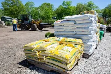 A worker stands near a front loader in a gravel lot next to bulk material bins